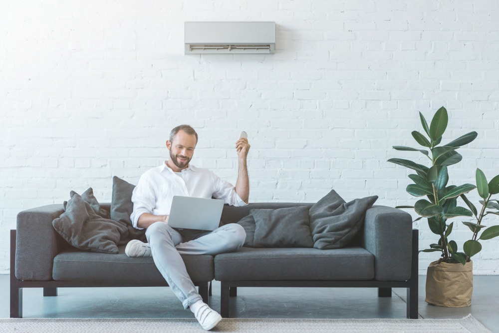 Man Turning On Air Conditioner with Remote Control — Air Conditioning Professionals in Forster, NSW