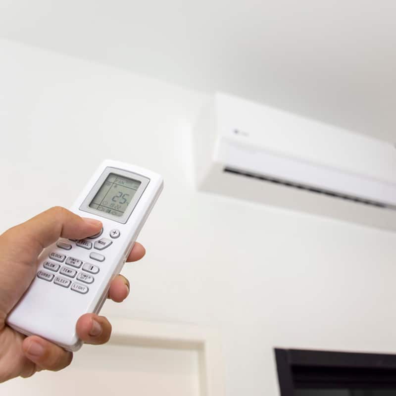Holding White Air Conditioner Remote — Air Conditioning Professionals in Forster, NSW