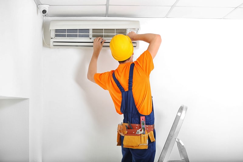 Male Technician Repairing Air Conditioner on the Wall — Air Conditioning Professionals in Pacific Palms, NSW